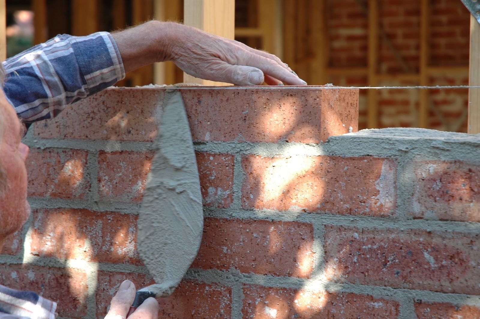 Mason pressing fresh mortar into ground joints with a tuck pointer